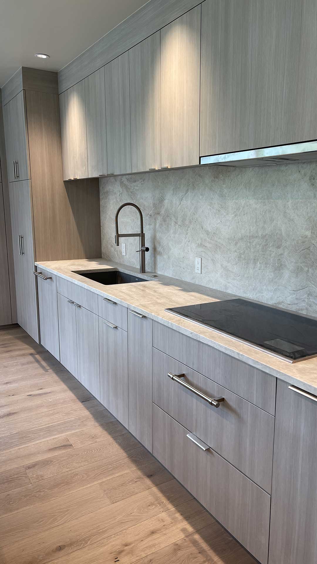 Gray Wood-Grain Kitchen — soft gray linear-grain cabinetry with Taj Mahal quartzite countertops and Wolf induction cooktop