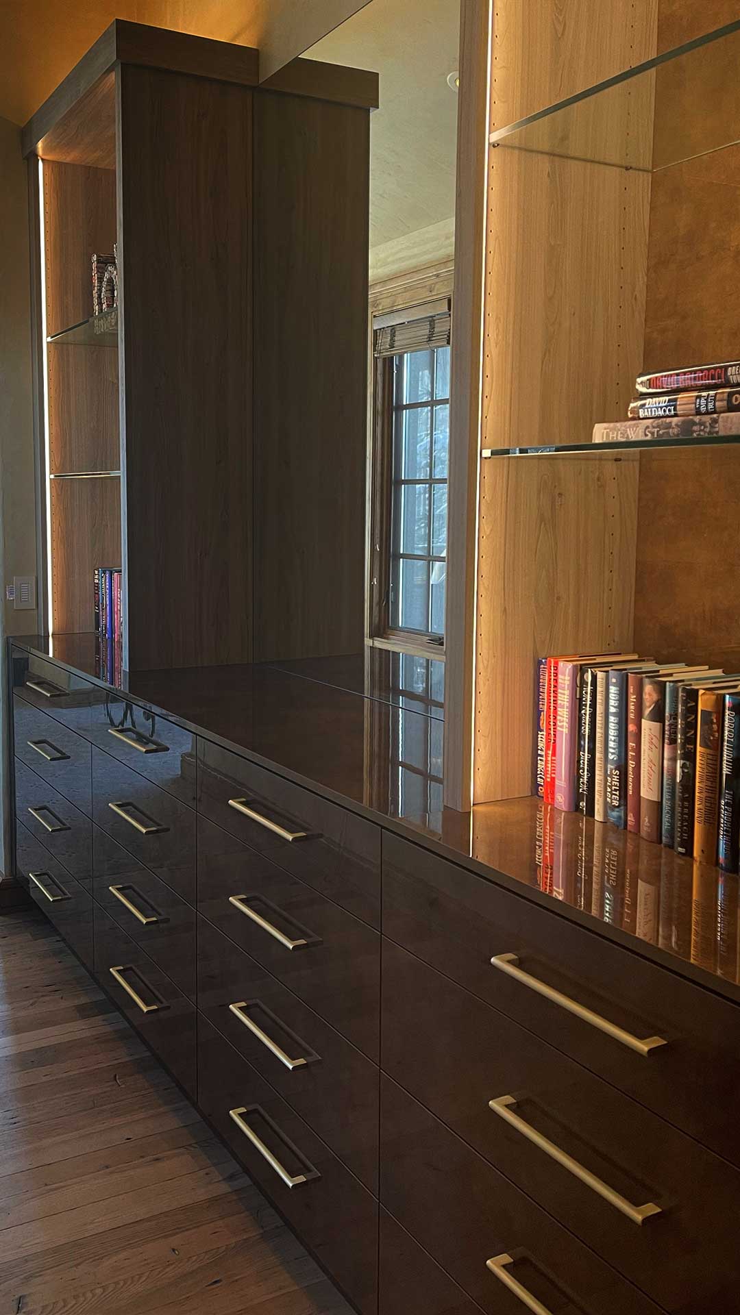 Built-In Dresser & Library Wall — Cuzco Oro cabinetry with glass display shelves, integrated LED lighting, and deep drawers